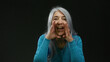 © Krakenimages.com - Grey-haired woman speaking expressively against black background, wearing blue sweater, conveying energy and emotion in an isolated scene of communication and expression.