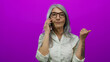 © Krakenimages.com - Senior woman with grey hair talks on smartphone and gestures with thumb against vivid pink background, wearing glasses and white shirt with tattoos on forearm.
