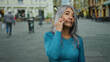 © Krakenimages.com - Grey-haired senior woman talking on phone outdoors in urban street setting with blurred buildings and pedestrians in background, wearing casual blue sweater.