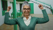 © Krakenimages.com - Senior woman with glasses and grey hair smiling and flexing arms in an outdoor street setting, embodying confidence and vitality during daytime.