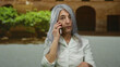 © Krakenimages.com - Senior woman with grey hair on a call outside an old university setting, gesturing expressively, highlighting a serene yet engaged outdoor communication moment.