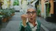 © Krakenimages.com - Senior woman with grey hair and glasses expressing anger on an outdoor urban street with colorful buildings in the background.
