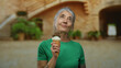 © Krakenimages.com - Woman enjoying ice cream outdoors at old university, showcasing the serene moment of a senior lady in a casual setting with historic charm in the background.
