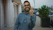 © Krakenimages.com - Man wearing glasses and a denim shirt holds up two fingers while smiling at camera on city street; joy friendly approachable relaxed.