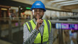 © Krakenimages.com - Man in blue hardhat and neon high visibility vest with finger to chin gesture in busy shopping mall building; confidence.
