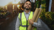 © Krakenimages.com - Man in neon safety vest holding rolled plans and makes ok sign on street near building and plants; confidence reliability expertise.