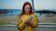© Krakenimages.com - Woman with red hair counting us dollars at a lively beach setting wearing a yellow sweater while people enjoy the seaside in the background.