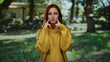 © Krakenimages.com - Woman standing in a sunlit park with red hair and a warm smile wearing a mustard sweater, surrounded by lush greenery and trees, enjoying a peaceful outdoor moment.