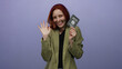 © Krakenimages.com - Redhead woman smiling and waving while holding italian passport against isolated purple background showcasing travel and identification.