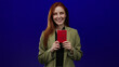 © Krakenimages.com - Woman holding swiss passport smiling in front of isolated blue background showcasing identification travel document adult redhead female attractive
