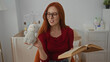 © Krakenimages.com - Woman with red hair and glasses smiling holding plush toy and book in cozy baby room with crib and dresser.