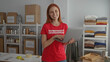© Krakenimages.com - Woman volunteer with laptop in donation center room wearing red shirt smiling surrounded by boxes and supplies for charity work indoors.