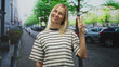 © Krakenimages.com - Blonde middle aged smiling woman holding up two fingers with right hand in peace sign on street wearing striped tshirt; cheerful.