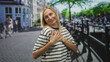 © Krakenimages.com - Woman smiling with outstretched hands and palms forward on a street beside a bicycle lined canal bridge, wearing a striped shirt and casual pose; warm welcome joy.