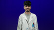 © Krakenimages.com - Man in white coat with name tag stands against a vivid blue background, exuding a professional yet approachable demeanor, pens visible in his pocket.