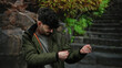 © Krakenimages.com - Hispanic man in a green jacket playfully miming on an urban street with stone stairs and lush greenery in the background, embodying a fun and dynamic city atmosphere.