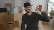 © Krakenimages.com - Young man smiling indoors holding keys in a new home surrounded by moving boxes and plants, representing a fresh start in an apartment setting.