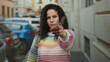 © Krakenimages.com - Woman with curly hair wearing rainbow sweater stands outdoors crossing arms and showing rejection on a city street with parked cars in the background.