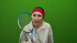 © Krakenimages.com - Young woman holding tennis racket looking surprised against isolated green background wall in studio setting showcasing sports and emotion.