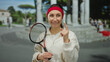 © Krakenimages.com - Young woman in athletic attire gestures idea with a tennis racket on a city street against a blurred outdoor urban backdrop, embodying confidence and determination.