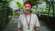 © Krakenimages.com - Young woman with medal and red headband stands in park, displaying a puzzled expression, surrounded by greenery, sunlight, and trees in a casual outdoor setting.