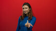 © Krakenimages.com - Young woman gesturing on isolated red background wearing blue sweater, creating inviting and approachable atmosphere with her smile and confident posture.