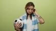 © Krakenimages.com - Woman holding soccer ball with pensive expression stands against yellow wall, sporting casual attire and scarf, embodying youthful sports enthusiasm and introspection.