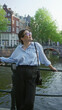 © Krakenimages.com - Woman standing on amsterdam canal bridge, smiling in blue shirt, enjoying outdoors, surrounded by green trees and traditional architecture.