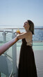 © Krakenimages.com - Woman holding iced drink with straw while leaning on wooden rail on cruise ship deck, bare shoulder visible and smiling toward sea; relaxation.