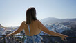 © Krakenimages.com - Woman brunette leaning on metal railing showing bare back and outstretched arms at building viewpoint over santorini town and caldera; serenity.