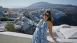 © Krakenimages.com - Woman leaning on a white wall at a santorini building viewpoint, smiling and raising one arm in a relaxed pose; serenity travel.