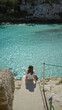 © Krakenimages.com - Woman enjoying view of cala llombars beach with turquoise waters in mallorca on a sunny day, highlighting the tranquility and natural beauty of the mediterranean coast.