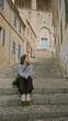 © Krakenimages.com - Woman sitting on stone steps in old mediterranean town of mallorca, wearing casual outfit, smiling, surrounded by historic architecture under sunny weather.