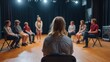 © 69 - Woman Sitting on Stage with Group of People in a Theater Setting During a Performance or Workshop
