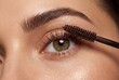 © Meow Creations - Close up detail of young woman applying mascara to eyelashes with brush showing natural skin texture