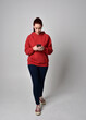 © faestock - full length figure of female model wearing  basic contemporary casual clothing, red hoodie jumper, skinny jeans, sneakers. standing walking pose holding cell phone mobile,  isolated white studio backg