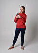 © faestock - full length figure of female model wearing  basic contemporary casual clothing, red hoodie jumper, skinny jeans, sneakers. standing walking pose holding cell phone mobile,  isolated white studio backg