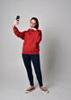 © faestock - full length figure of female model wearing  basic contemporary casual clothing, red hoodie jumper, skinny jeans, sneakers. standing walking pose holding cell phone mobile,  isolated white studio backg
