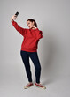 © faestock - full length figure of female model wearing  basic contemporary casual clothing, red hoodie jumper, skinny jeans, sneakers. standing walking pose holding cell phone mobile,  isolated white studio backg