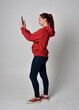 © faestock - full length figure of female model wearing  basic contemporary casual clothing, red hoodie jumper, skinny jeans, sneakers. standing walking pose holding cell phone mobile,  isolated white studio backg