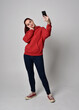 © faestock - full length figure of female model wearing  basic contemporary casual clothing, red hoodie jumper, skinny jeans, sneakers. standing walking pose holding cell phone mobile,  isolated white studio backg
