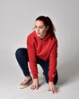 © faestock - full length figure of female model wearing  basic contemporary casual clothing, red hoodie jumper, skinny jeans, sneakers.  kneeling on floor  isolated white studio background.