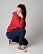 © faestock - full length figure of female model wearing  basic contemporary casual clothing, red hoodie jumper, skinny jeans, sneakers.  kneeling on floor  isolated white studio background.