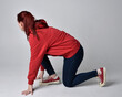 © faestock - full length figure of female model wearing  basic contemporary casual clothing, red hoodie jumper, skinny jeans, sneakers.  kneeling on floor  isolated white studio background.