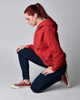 © faestock - full length figure of female model wearing  basic contemporary casual clothing, red hoodie jumper, skinny jeans, sneakers.  kneeling on floor  isolated white studio background.