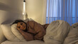 © Evgeniia Primavera - Young woman lying on bed at night with sad expression low mood dim bedroom light emotional exhaustion mental health struggle isolation loneliness depression concept fatigue insomnia