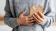 © Bonsales - Person feeling stomach discomfort, holding a bitten slice of bread, concept of gluten intolerance or indigestion