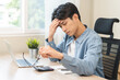 © KMPZZZ - Exhausted, asian young businessman work at office desk, male took off eye glasses, headache from migraine, suffer on work hard, using laptop computer at office home, overtime job. Health care concept.