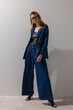 © Cumhur - Elegant modern woman wearing oversized denim blazer and wide leg jeans with leather top, posing confidently in minimalist studio. Fashion, lifestyle, business casual concept with copy space.