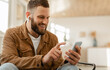 © Prostock-studio - Happy Man Using Mobile Phone Wearing Earbuds And Texting Sitting In Chair At Home. Guy Listening To Music And Networking In Social Media Via Smartphone Using Application. People And Gadgets